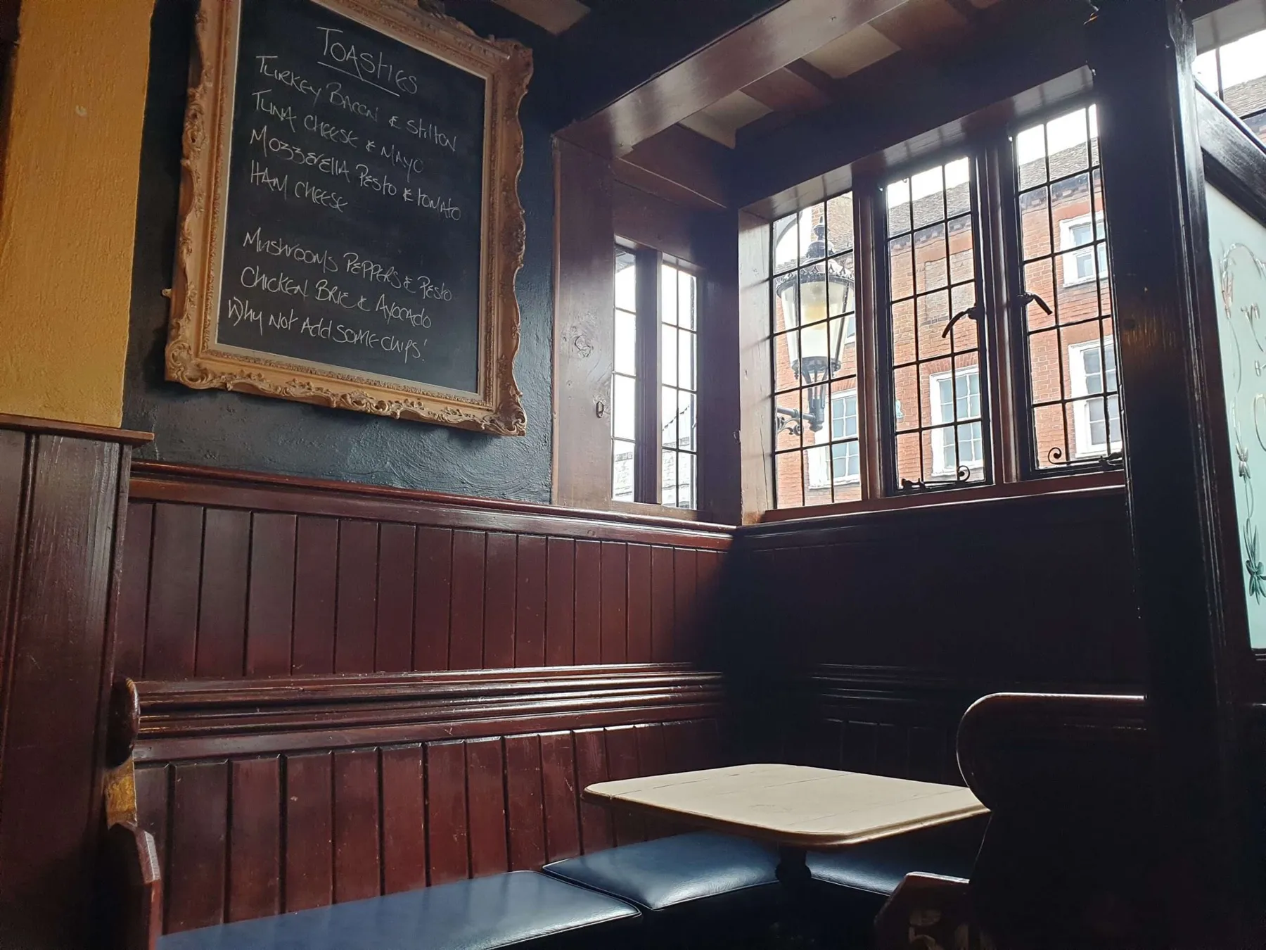 A booth by the leaded windows at The Nags Head bar, with the toasties chalkboard on the wall